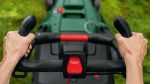Person, die den Griff eines grünen Rasenmähers auf Gras greift.