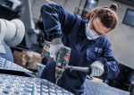 Arbeiter mit Schutzausrüstung bohrt mit einer Akku-Bohrmaschine in ein Metallblech.