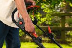 Person, die im Garten den Griff eines Akku-Rasenmähers einstellt.